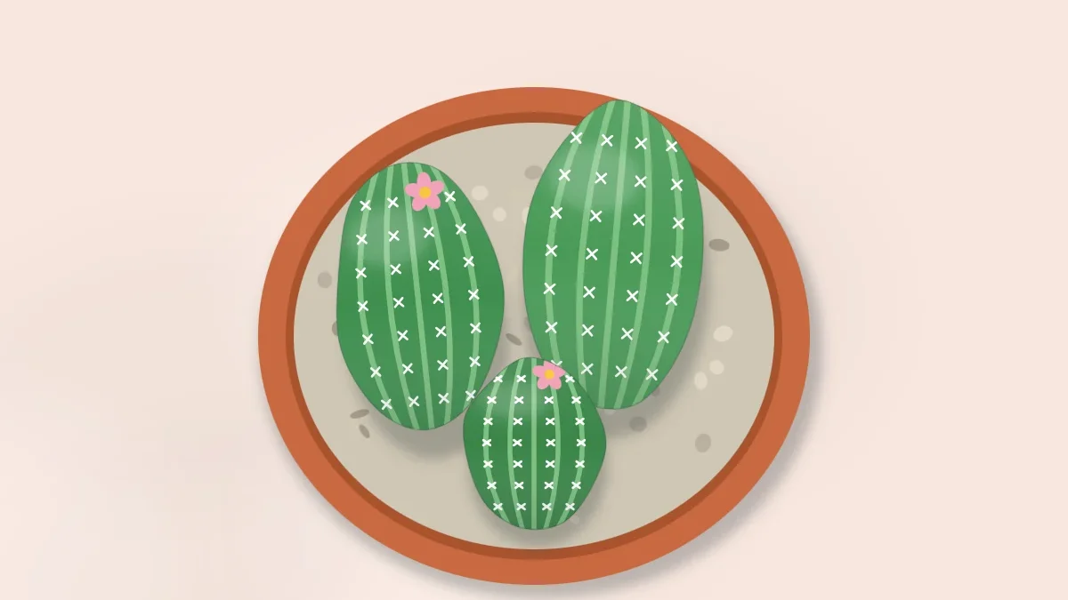 A terracotta pot filled with gravel holding three upright stones painted as green cacti with white spines, one with a small pink flower
