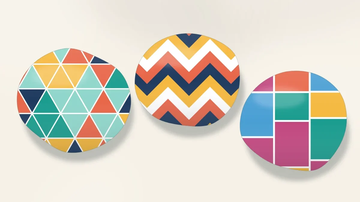 Three stones with crisp geometric designs: a mosaic of triangles, bold chevrons and color blocks divided by white lines