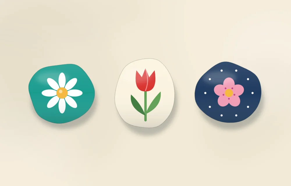 Three stones with different flower styles: a white daisy, a red tulip with a stem and two leaves, and a pink five-petal blossom