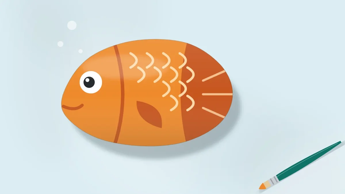 Oval stone painted as a bright orange fish with a tail, fin, scales and one round eye, on a pale blue surface with a brush beside it