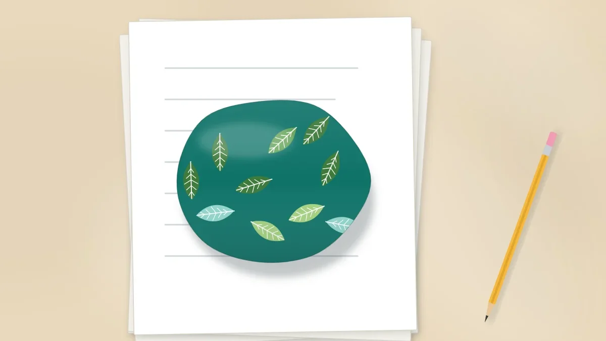 A large smooth stone painted with a leafy pattern sitting on a stack of paper sheets on a desk, with a pencil nearby