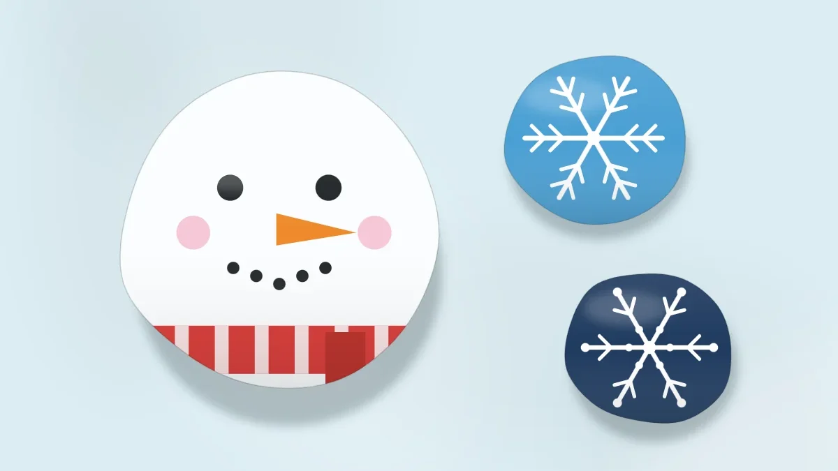 A white snowman face stone with a carrot nose and a red scarf, next to two blue stones painted with white snowflakes